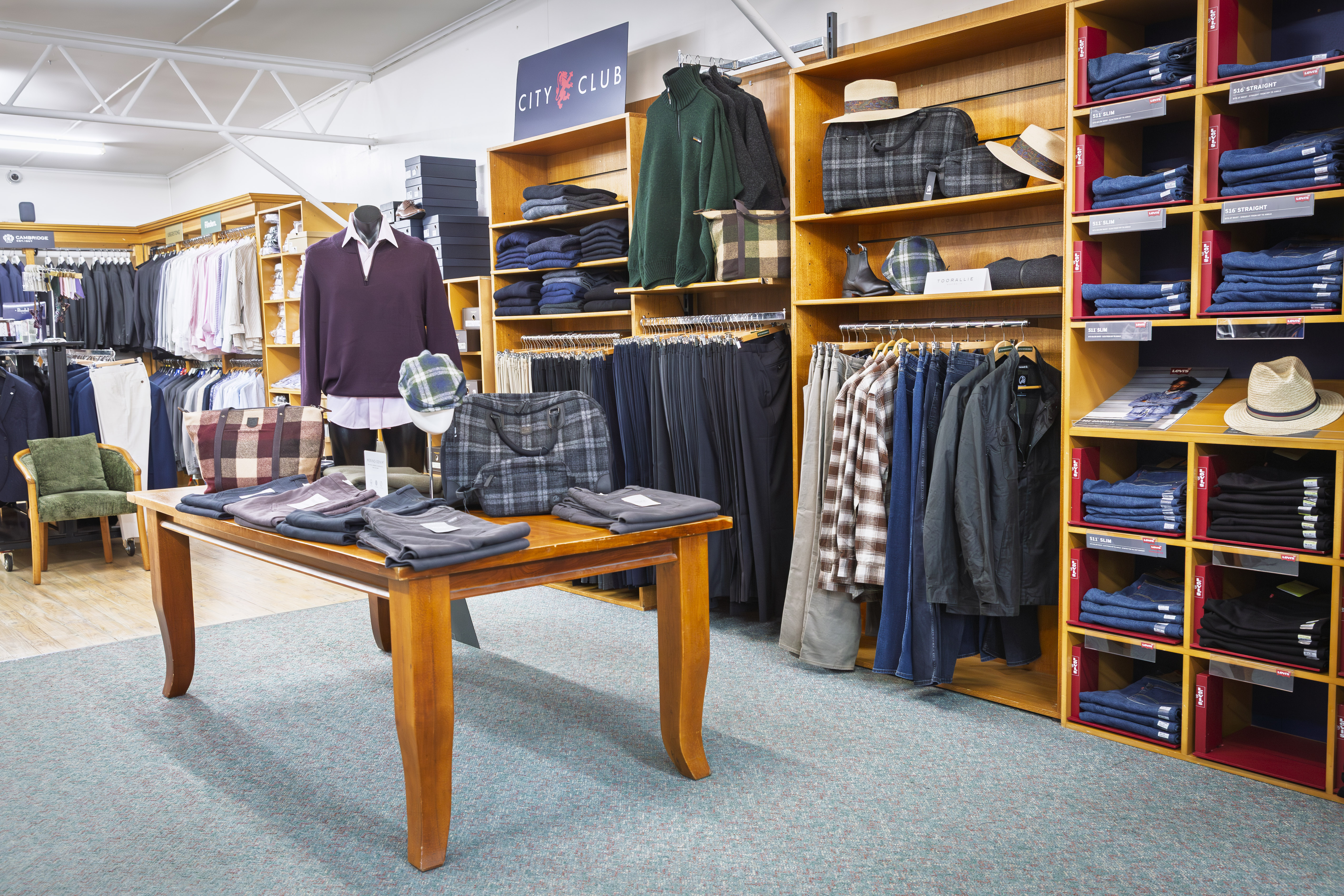 Menswear display table with folded clothing, hats and mannequin.