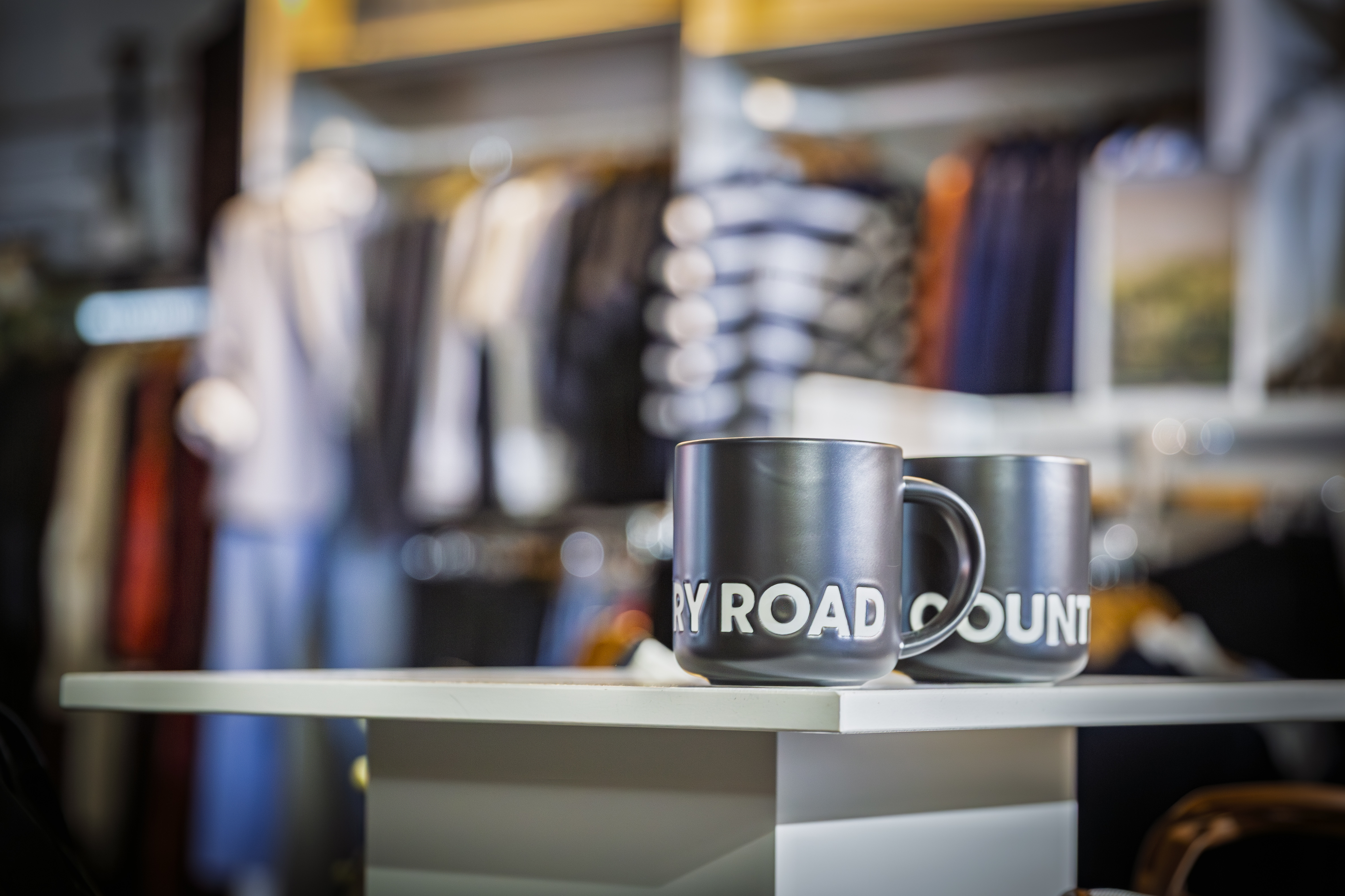 Country Road branded mugs with clothing racks in the background.
