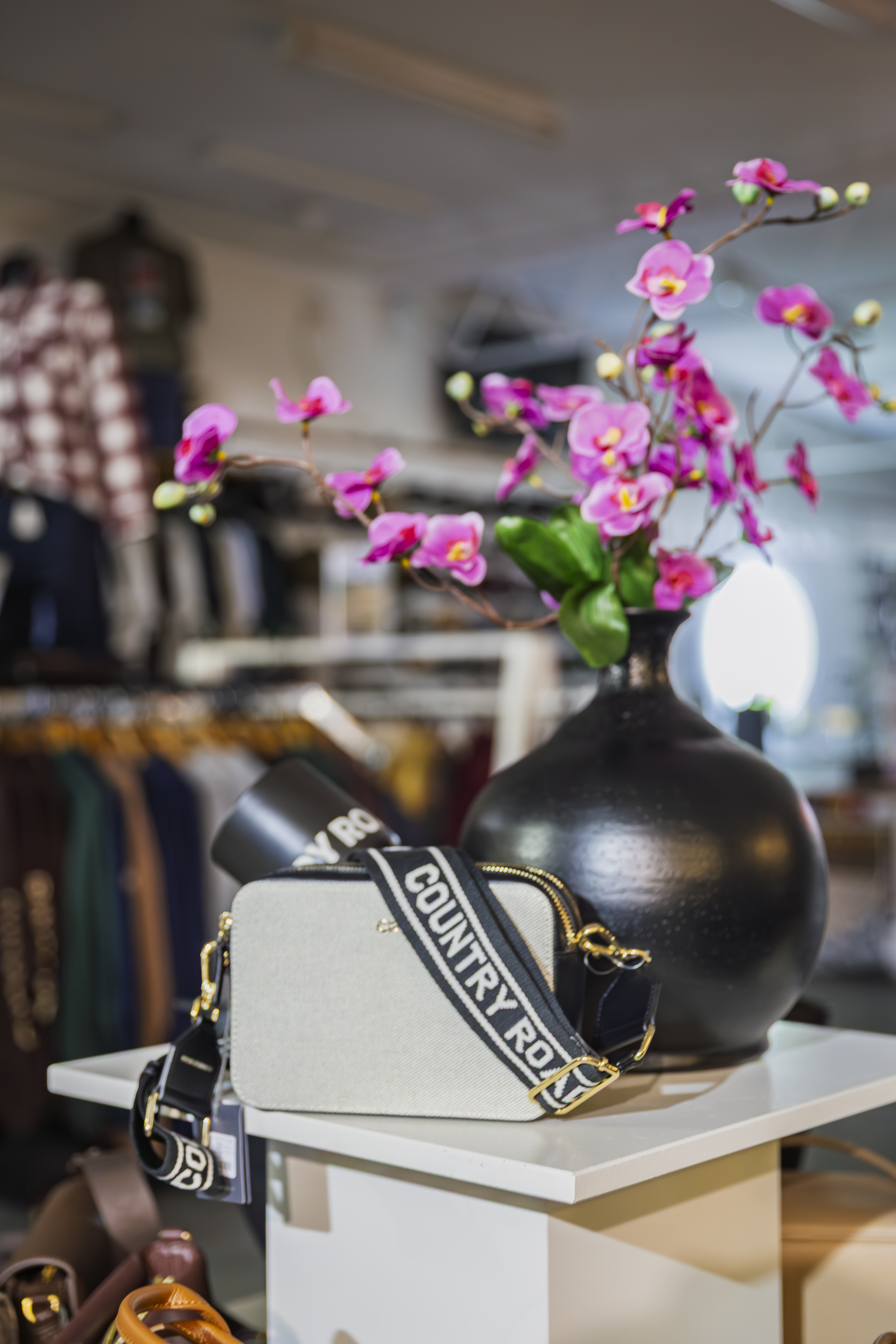 Accessories display with leather bags, cap and potted plants under Country Road signage.