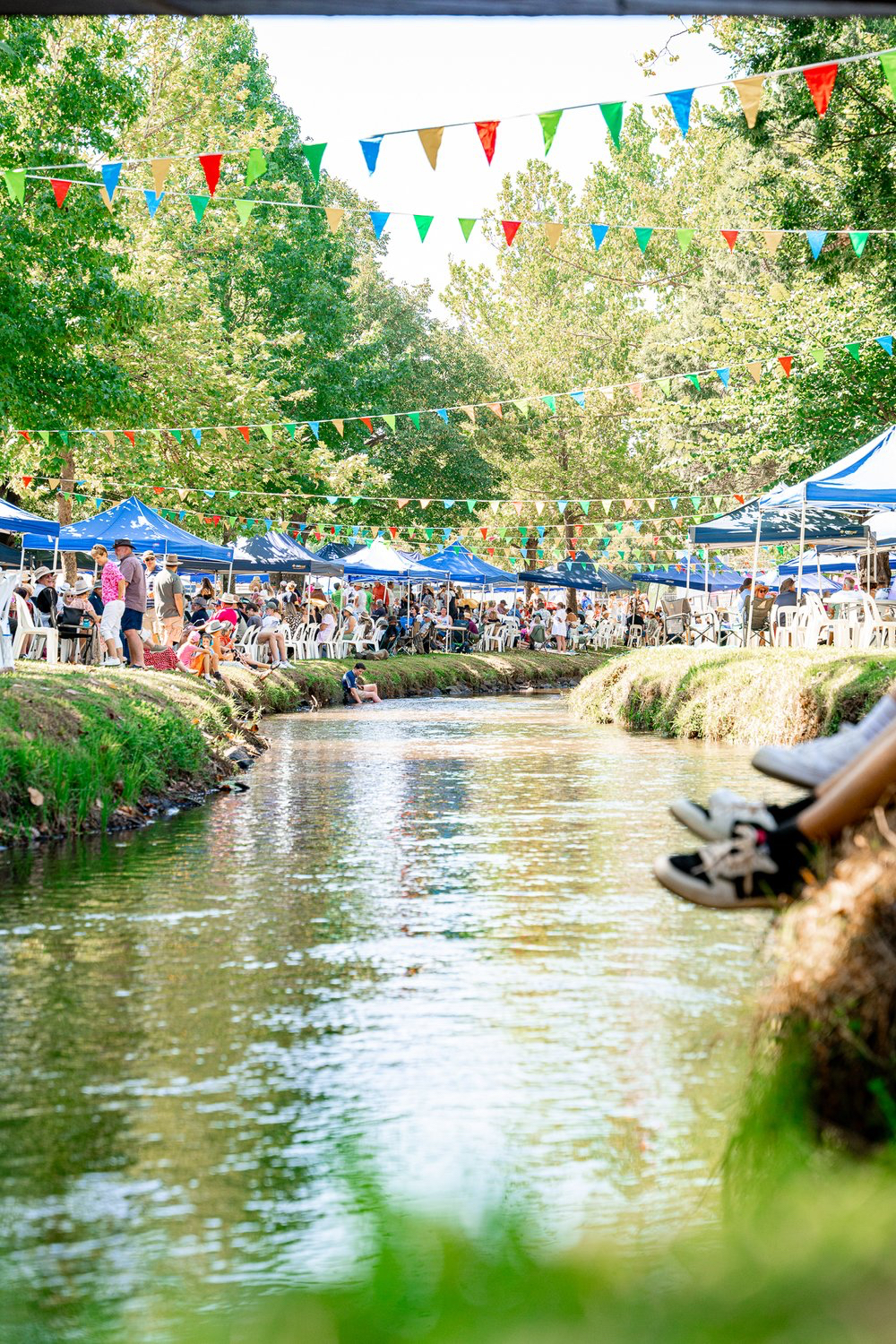 Festival by the creek in Tumut with colourful bunting overhead.